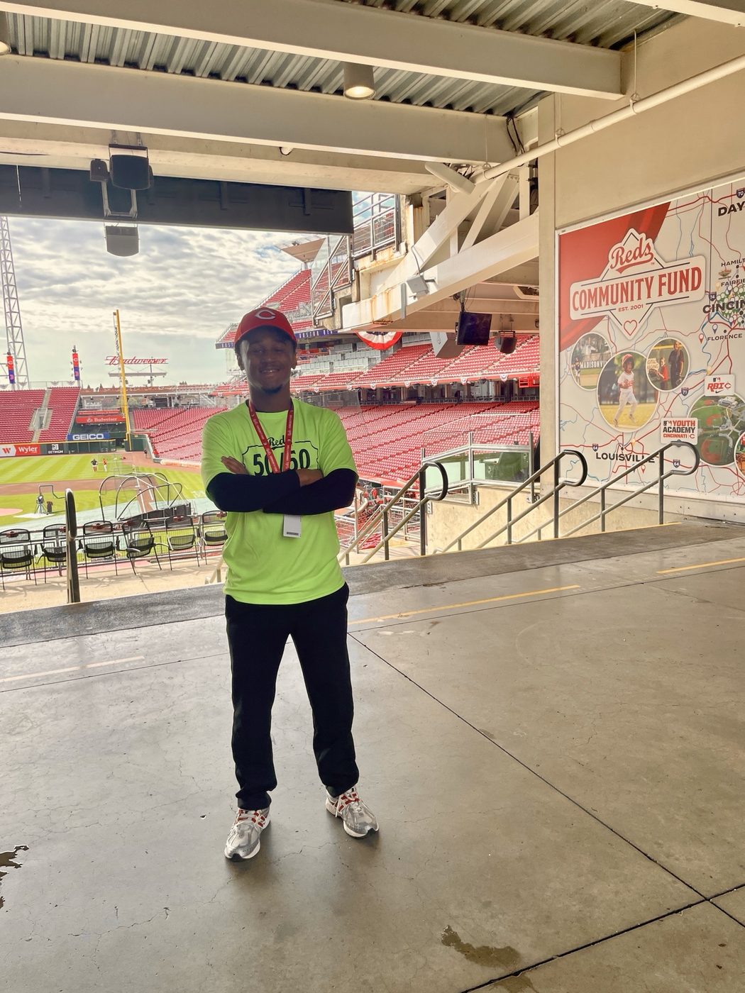 Yohan in a 50/50 raffle shirt in front of a Reds Community Fund sign, with the empty ballpark behind him